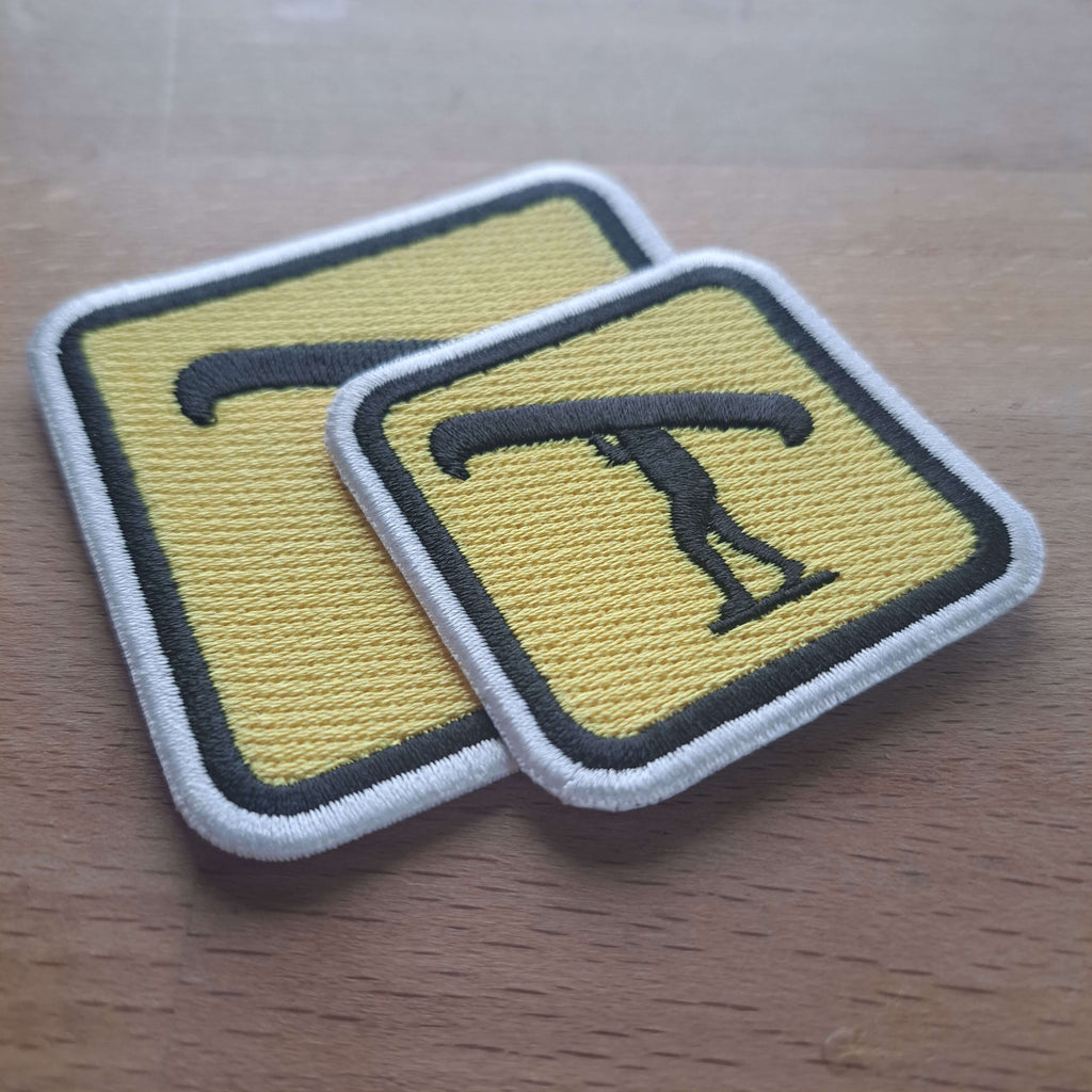 2 yellow and black embroidered patches of Canoehead portage sitting on a wooden desk